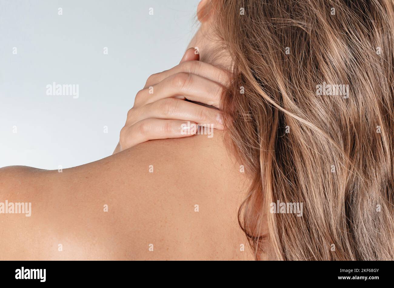 Woman with long blond hair holds  neck with hand. Rear view. Diseases of cervical spine, injuries, arthritis, scoliosis, pinched nerve. Stock Photo