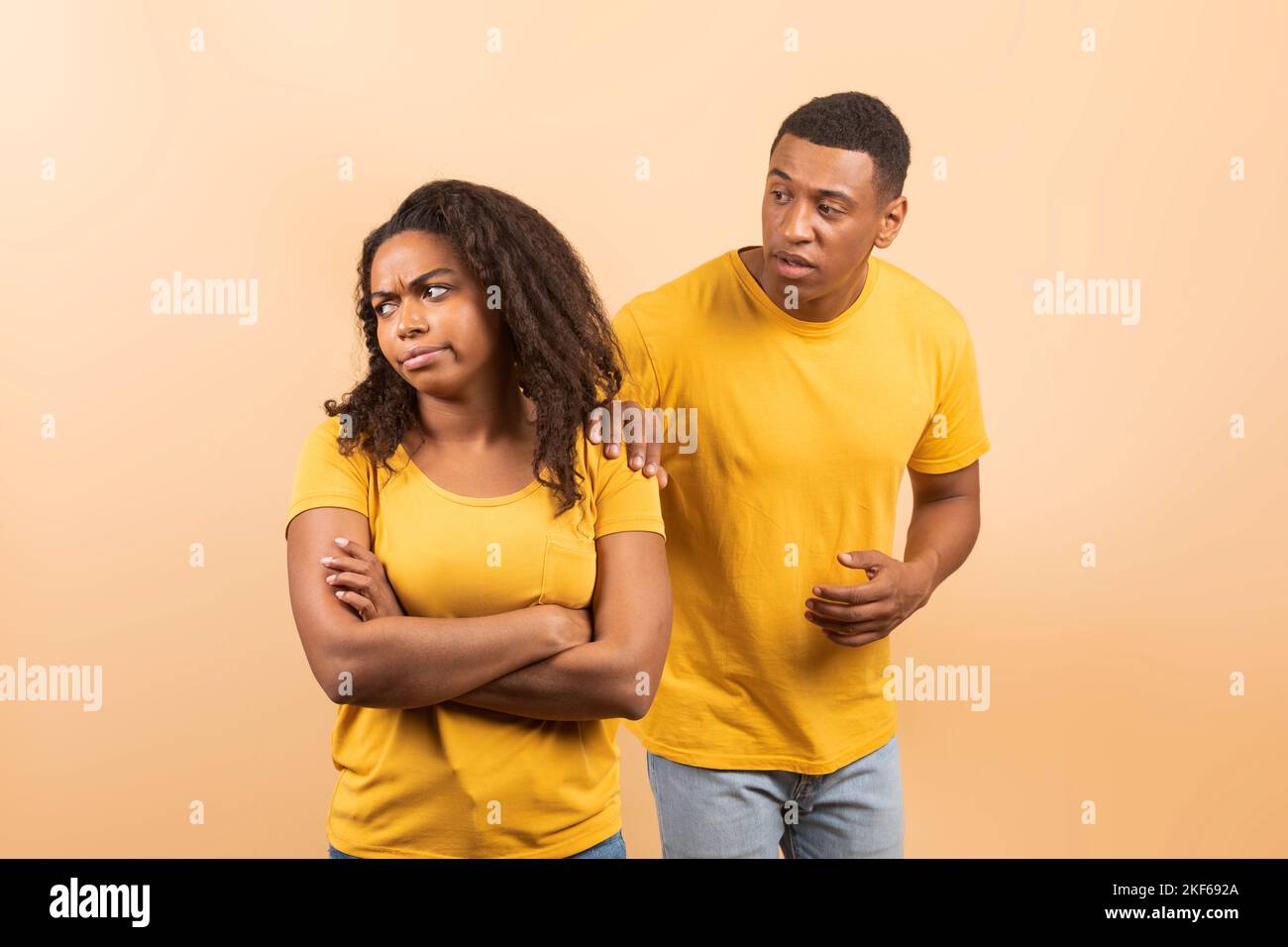 Black couple after quarrel, husband trying to talk and reconcile with offended wife, standing over peach background Stock Photo