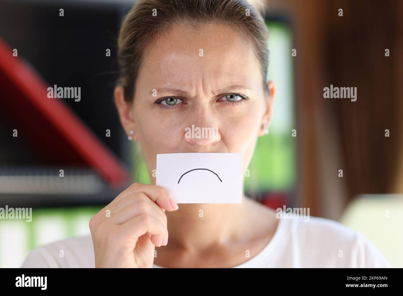 Depressed woman hides her mouth with white paper with sad sign. Stock Photo