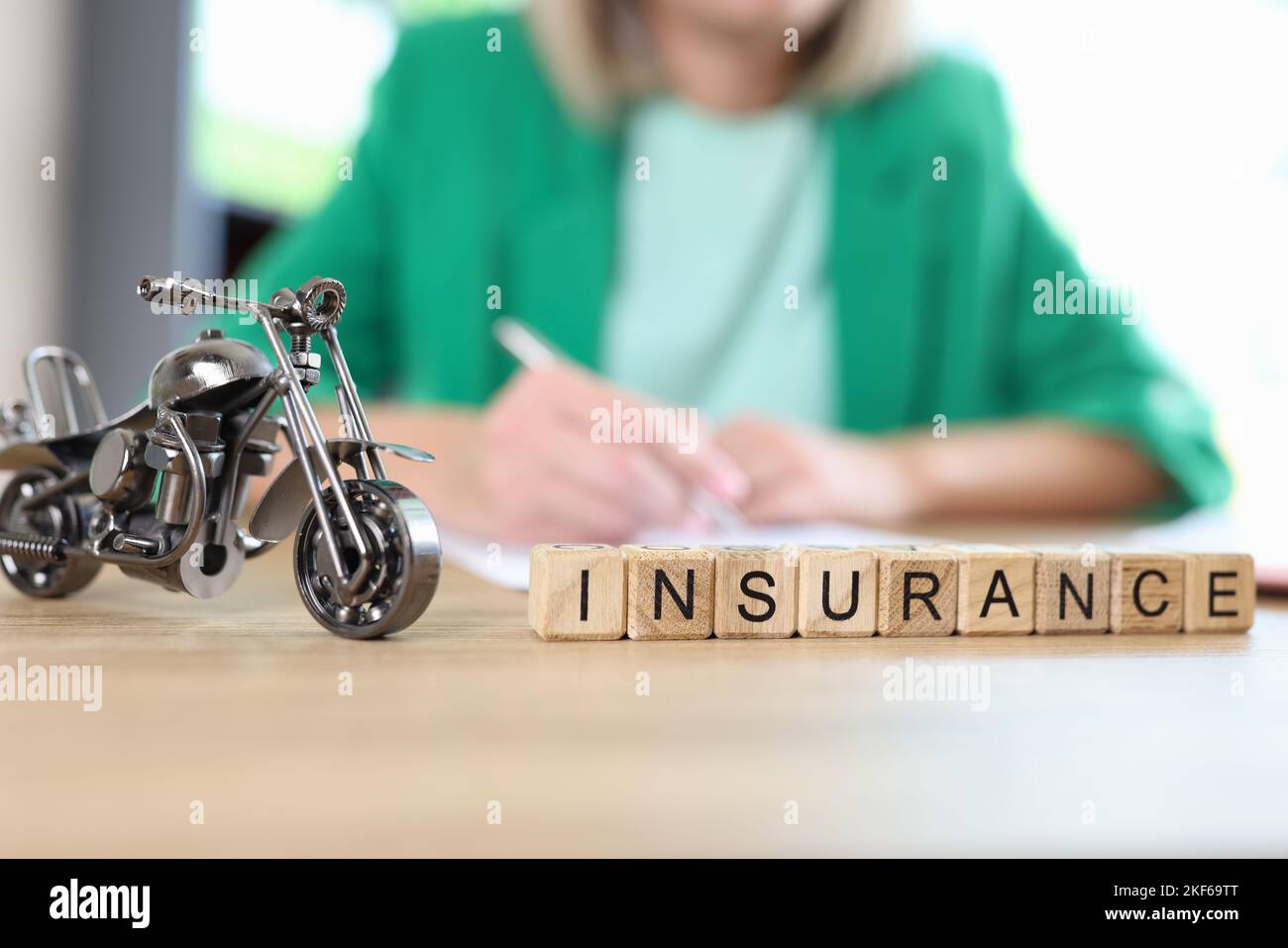 Motorcycle model and word insurance on table, blurred manager with documents in background. Stock Photo