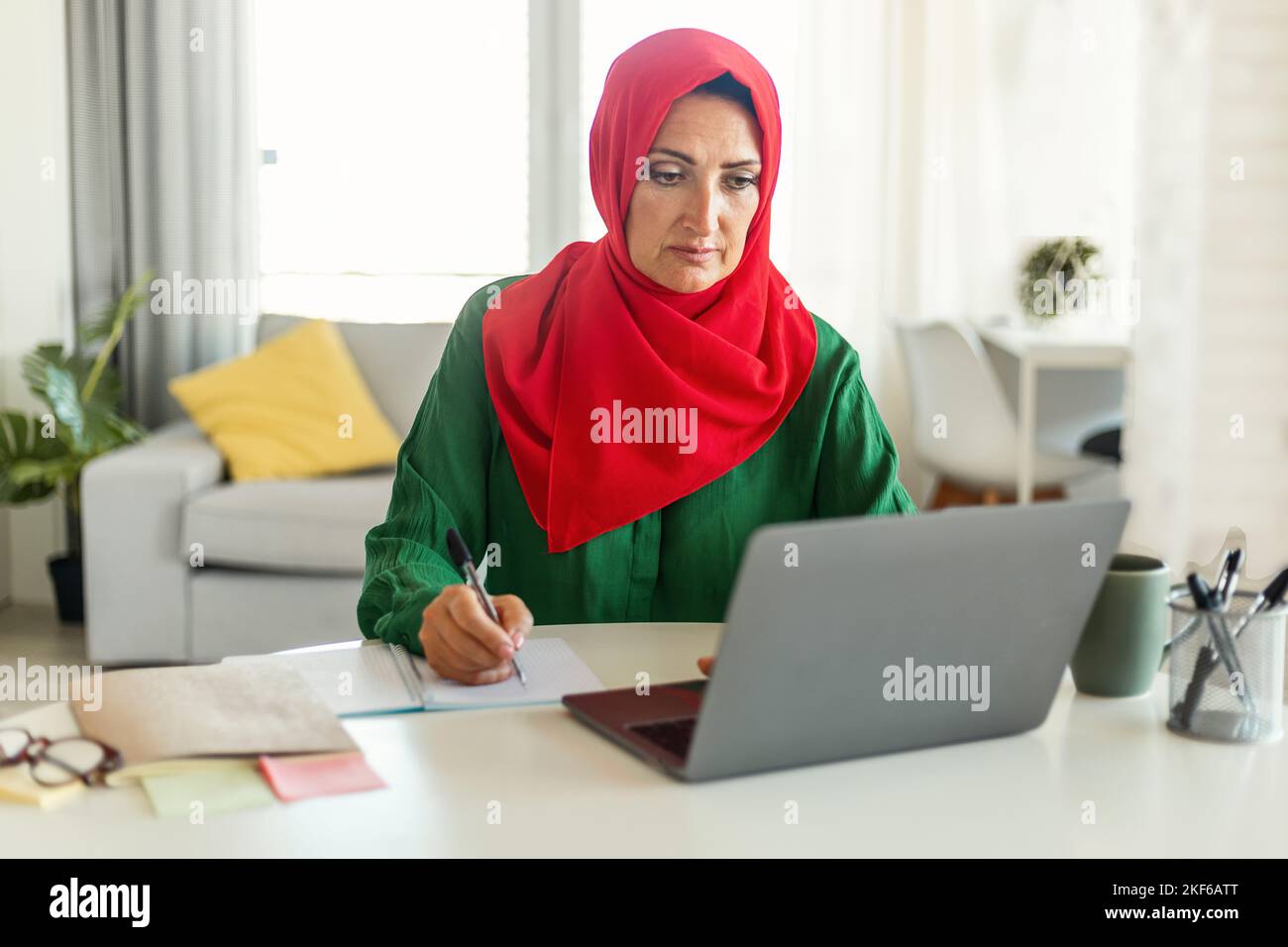 Focused muslim woman in hijab using laptop and calculating budget ...