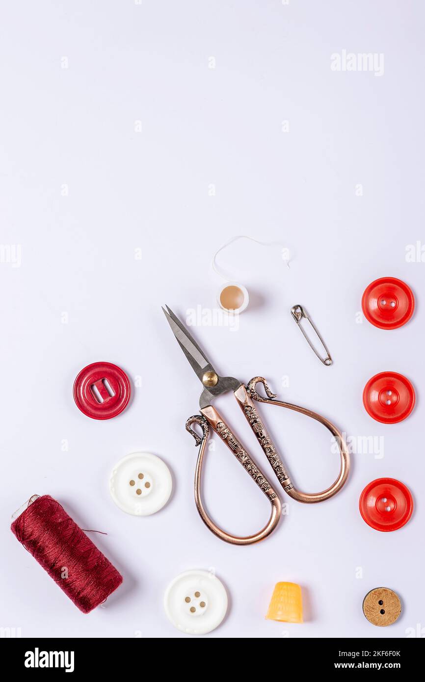 A composition of red sewing thread, thimble, vintage scissors, buttons and safety pin on a white background Stock Photo