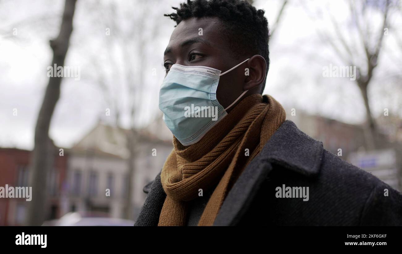 Black man walking outside during pandemic wearing surgical mask Stock ...