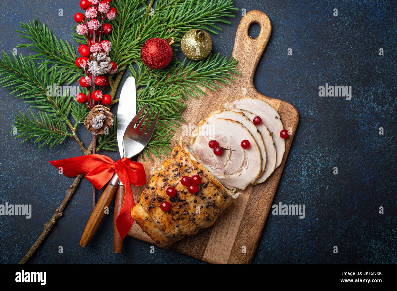 Christmas baked ham sliced with red berries and festive decorations Stock Photo