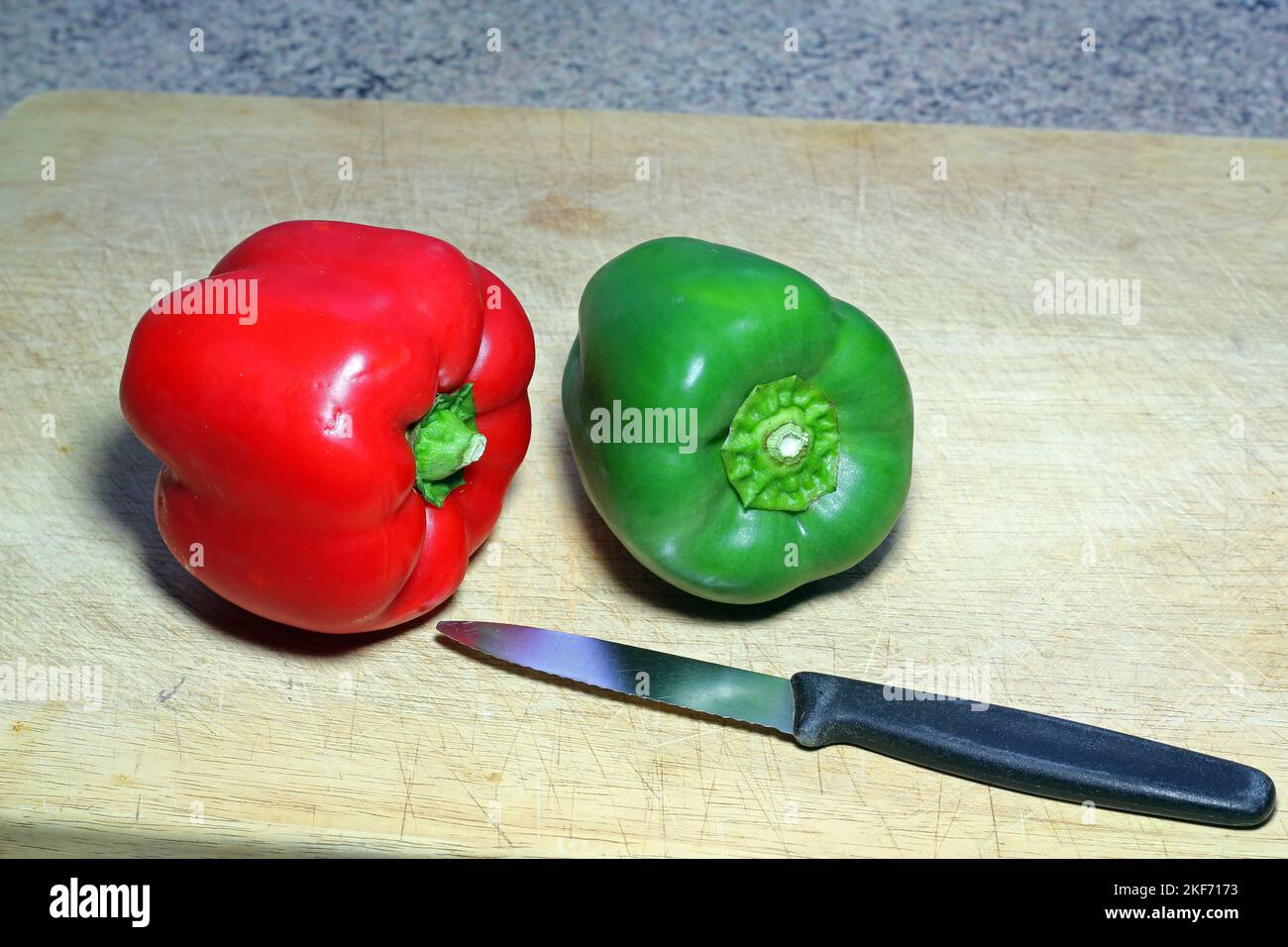 A green and red pepper on a work surface with a knife ready to be prepared. Stock Photo