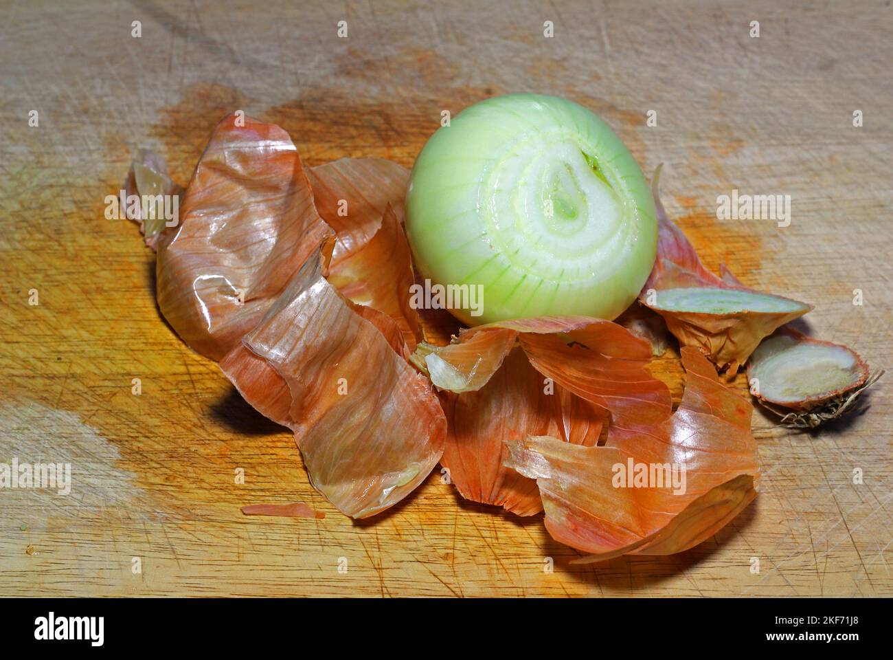 Peeled onion with the brown skin next to it. ready to chop on a wooden board. Stock Photo