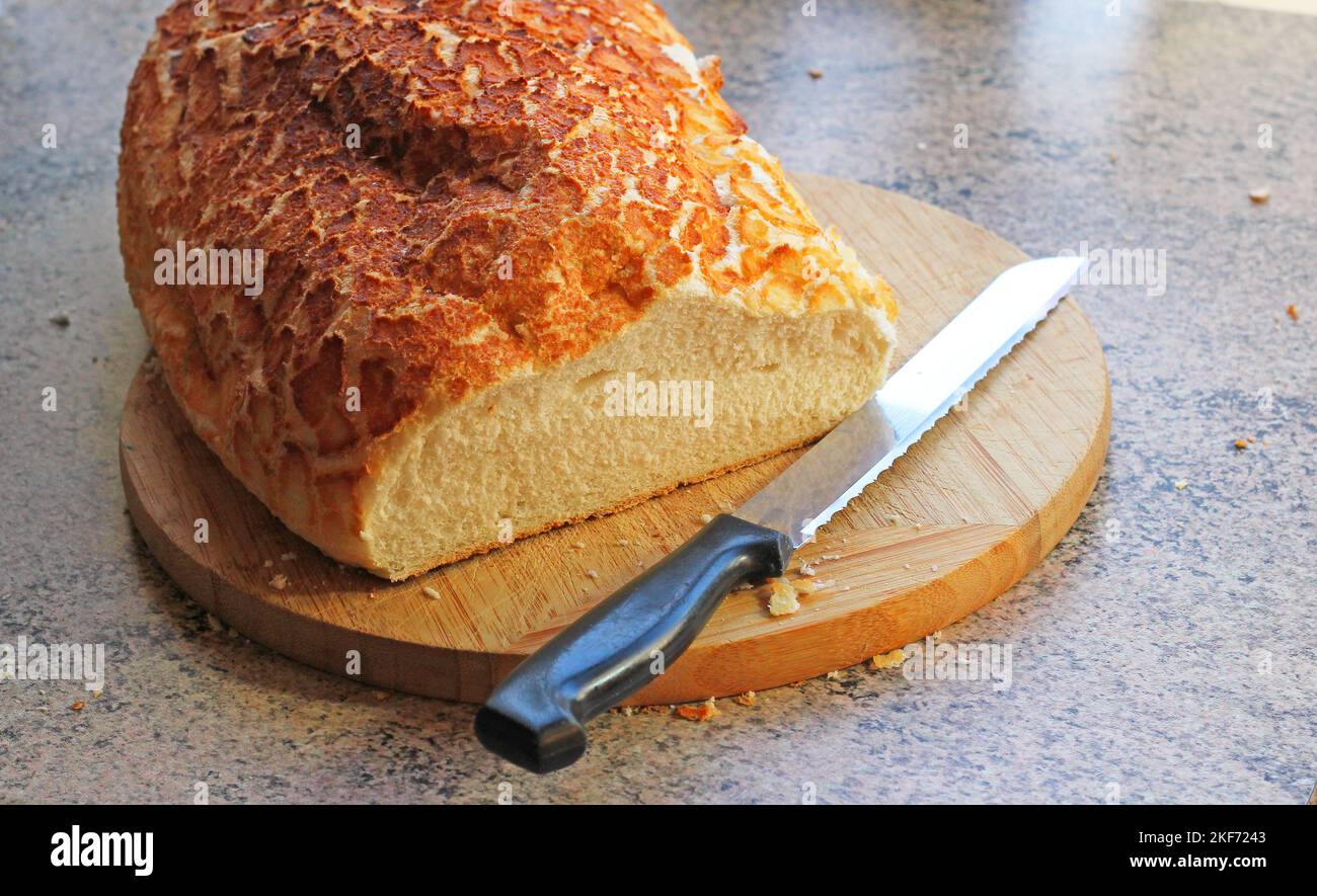 Uncut fresh loaf of bread on a bread board with a carving knife ready