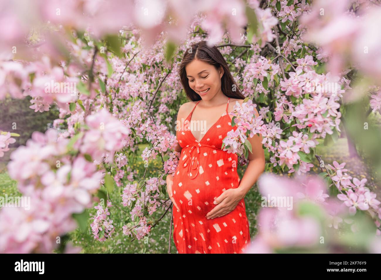 Pregnant woman happy portrait in with spring flowers. New season and new life concept. Pregnancy in 3rd trimester. Asian woman expecting baby feeling Stock Photo