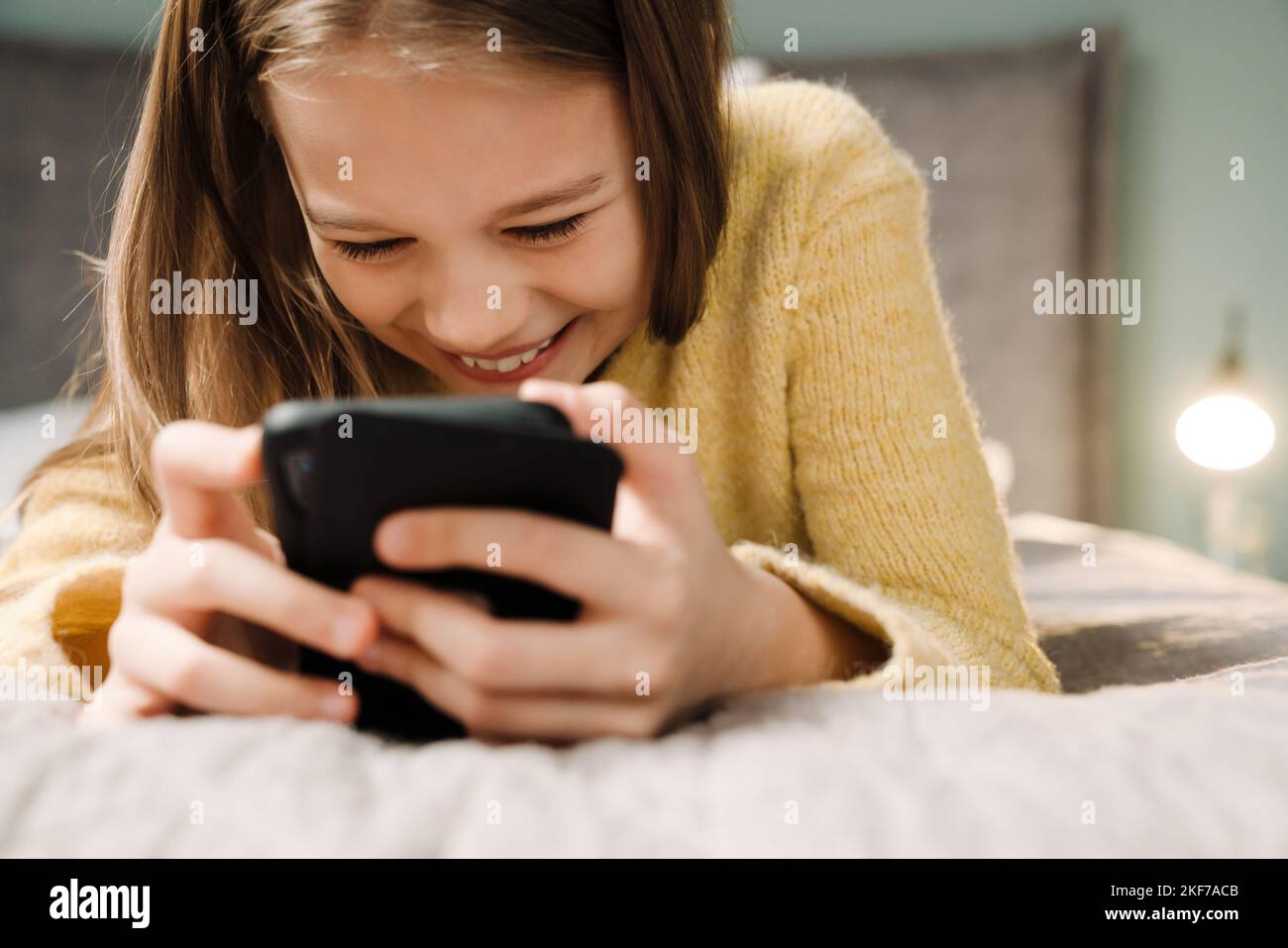 White happy girl using mobile phone while lying on bed at home Stock Photo