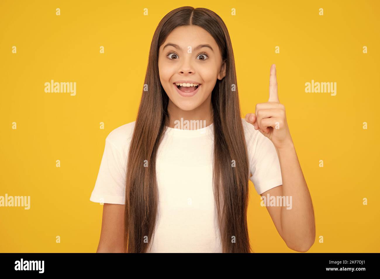 Happy teenager portrait. Funny face of young teenager pointing up with finger, isolated on yellow background. Girl has great new idea. Funny school Stock Photo