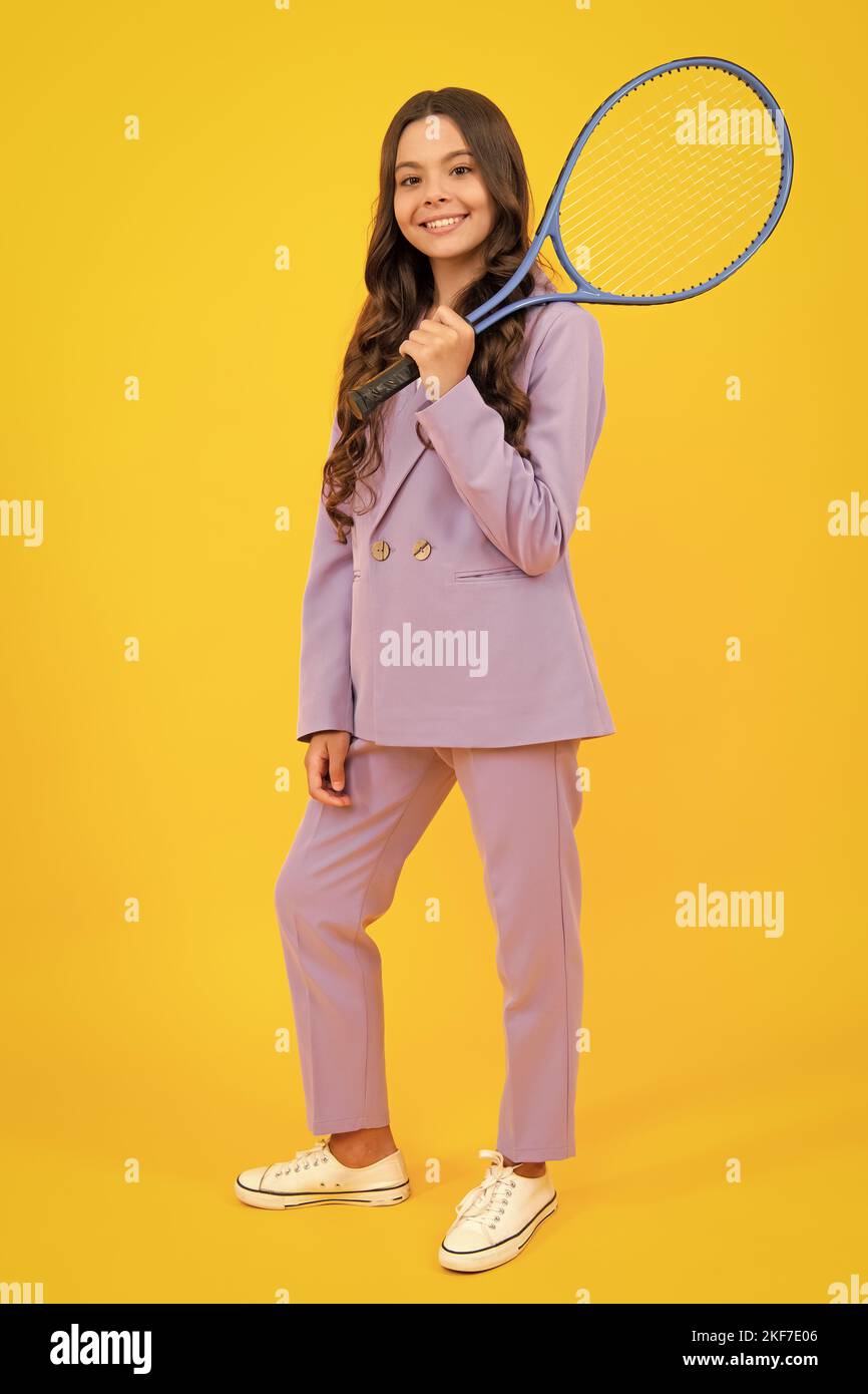 Fashion teenage tennis player girl in trendy suit hold tennis racket over isolated yellow background. Tennis school. Stock Photo