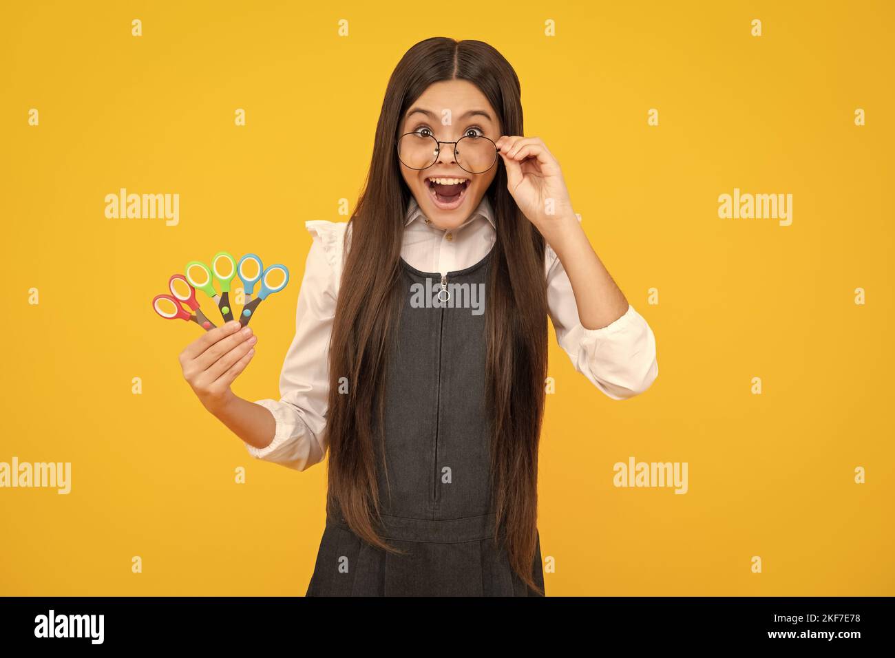 Excited amazed teenage girl with scissors, isolated on yellow background. Child creativity, arts and crafts. Stock Photo
