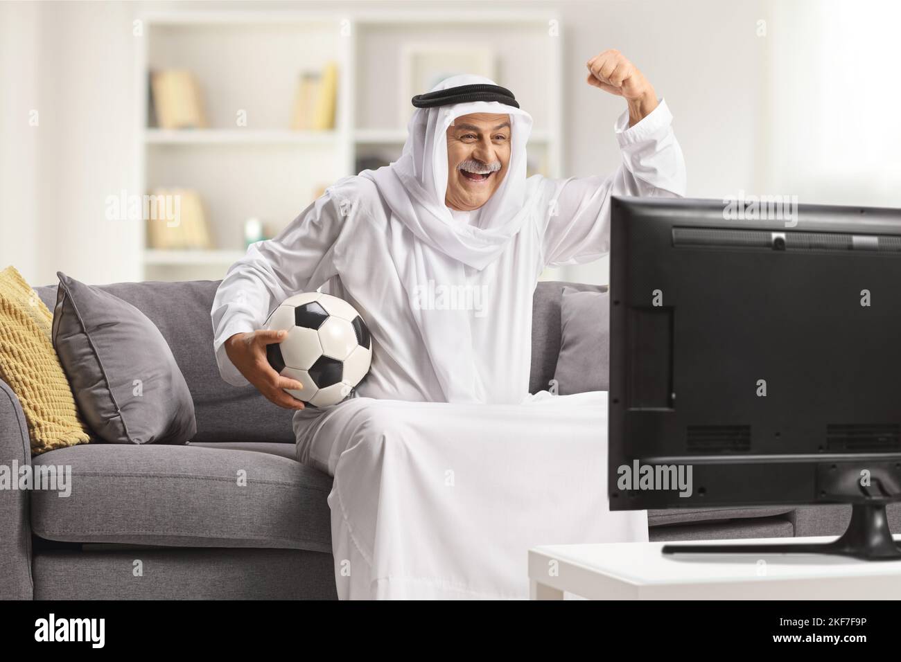 Mature arab man in a robe holding a football and cheering in front of tv at home Stock Photo