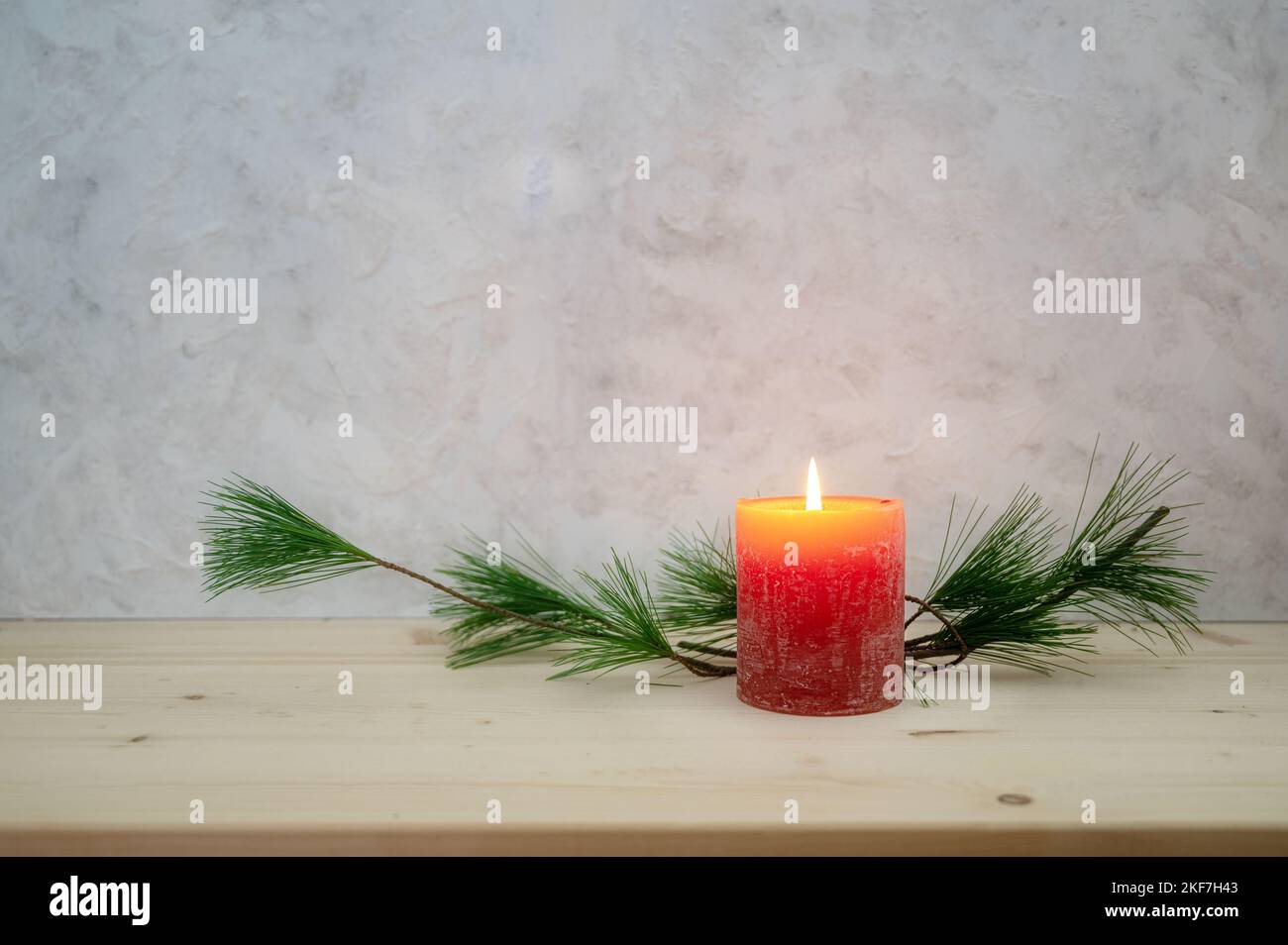 Red candle lit for the first Advent, pine branch as a simple, minimal decoration on a light wooden board against a rustic plaster wall, large copy spa Stock Photo