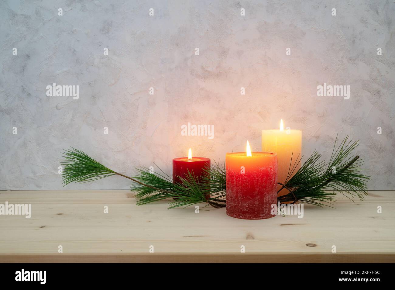 Three candles lit for the third Advent, pine branch as a simple, minimal decoration on a light wooden board against a rustic plaster wall, large copy Stock Photo