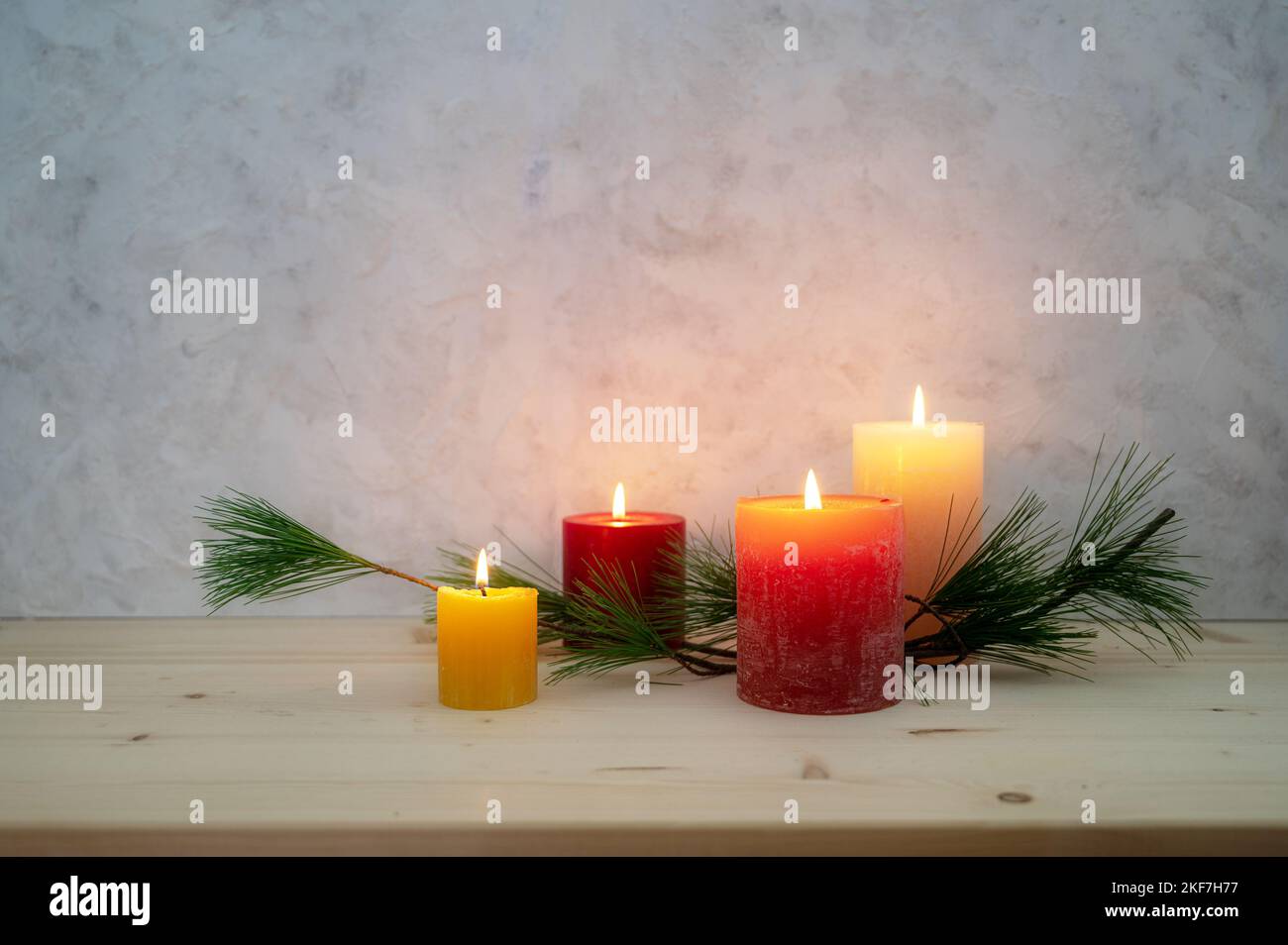 Four candles lit for the fourth Advent, pine branch as a simple, minimal decoration on a light wooden board against a rustic plaster wall, large copy Stock Photo