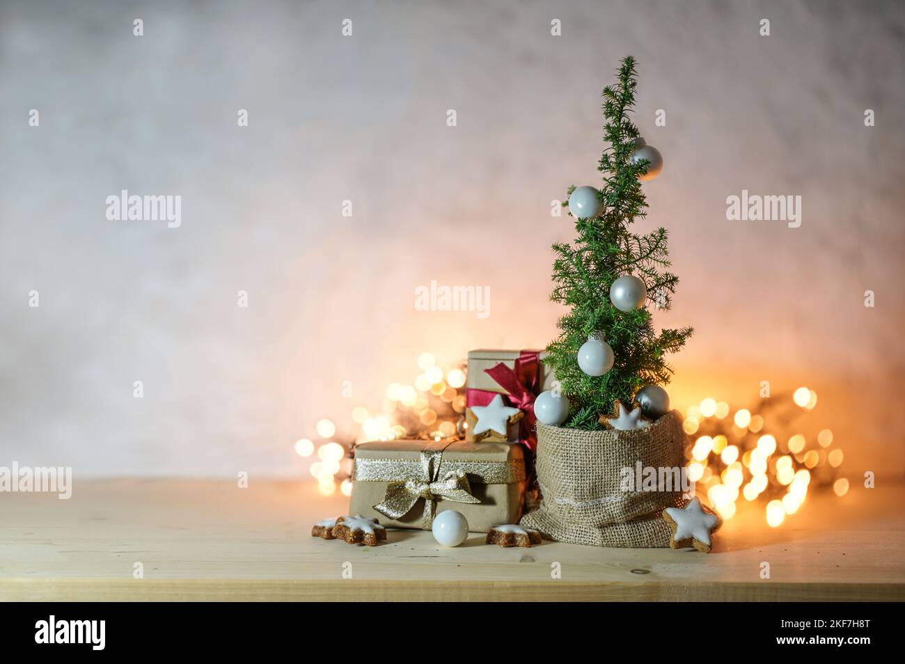 Alternative space saving Christmas tree, small potted conifer plant, decorated with baubles, stars and gifts in front of blurry fairy lights, large co Stock Photo
