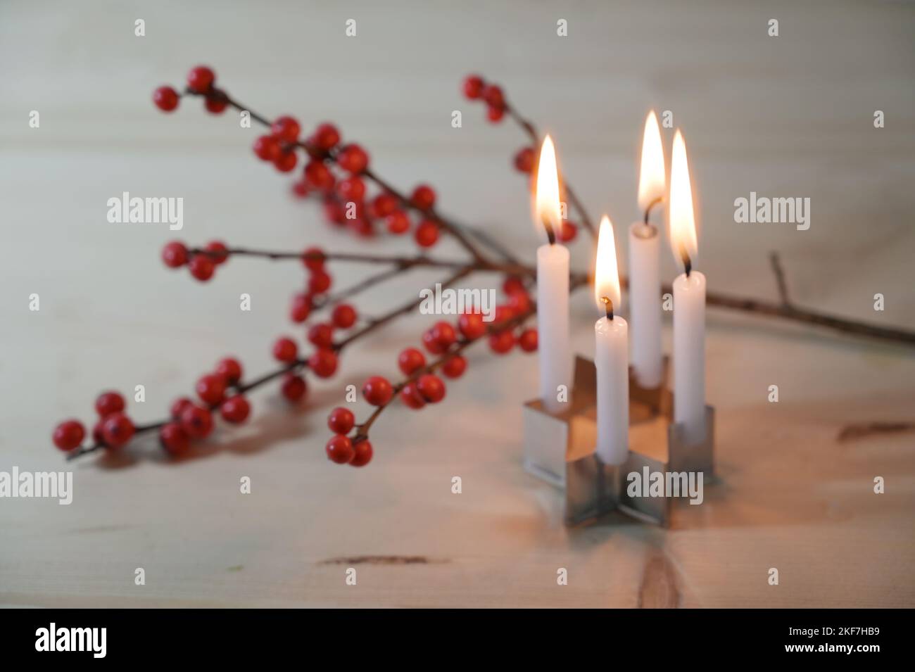 Mini advent wreath, four small candles on a cookie cutter in star shape in front of a holly branch with red berries on a wooden table, selected focus, Stock Photo