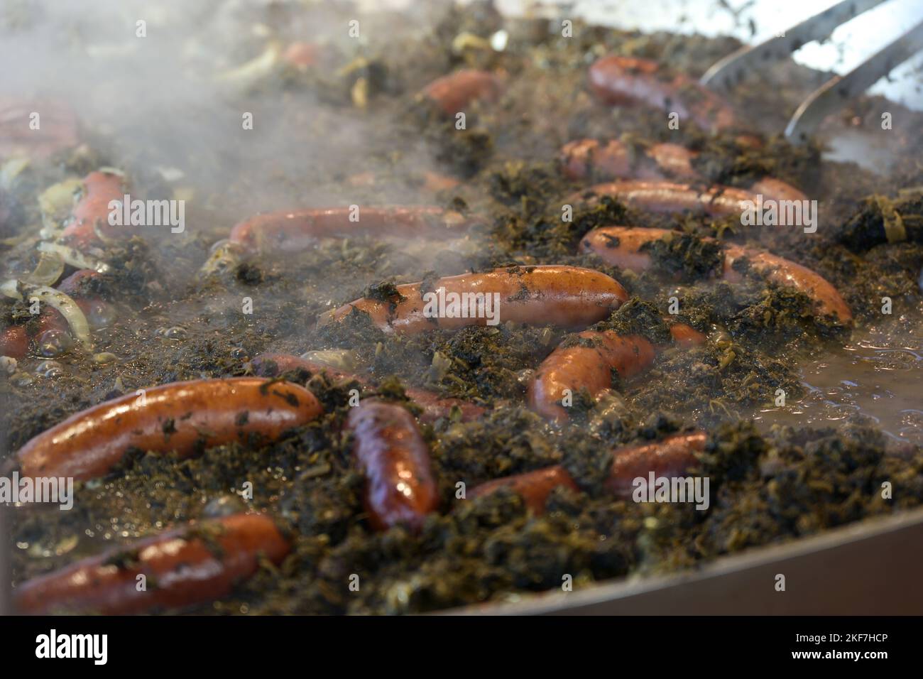 Large pot with steaming curly green kale and sausages at an autumn market, German street food in the cold season, selected focus, narrow depth of fiel Stock Photo