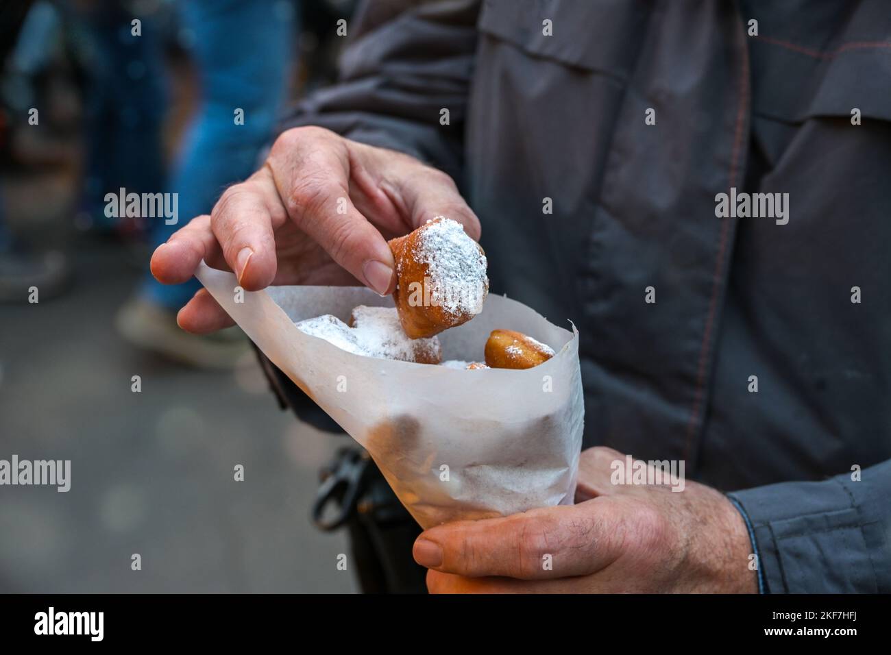 Hands of a man with a paper bag of Mutzenmandeln, deep fried sweet pastry with almonds covered with powdered sugar, traditional German fair snack on C Stock Photo