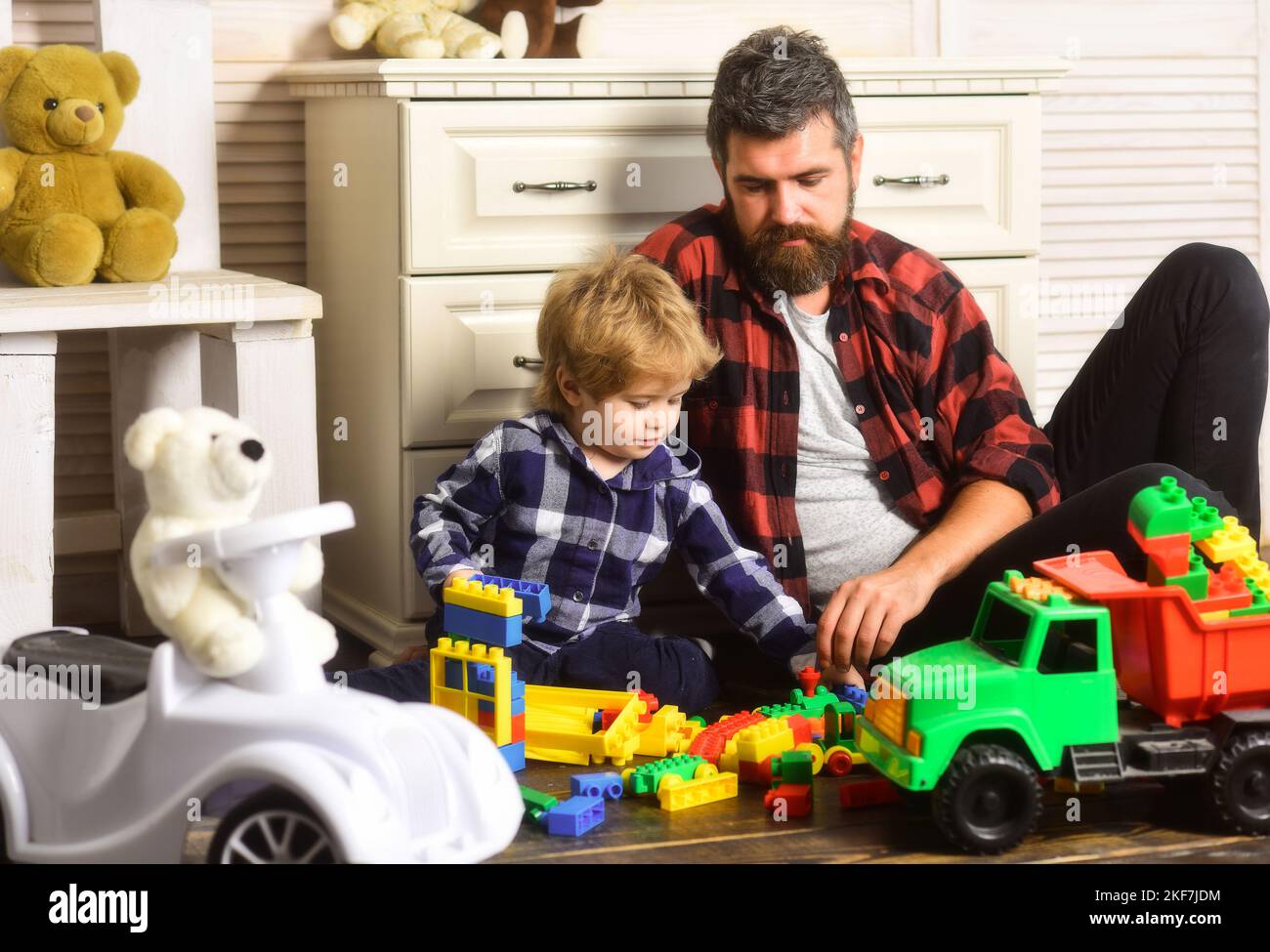 Father and son create toys from bricks. Dad and kid build of plastic blocks. Father and son playing toys wooden blocks on floor in living room. Stock Photo