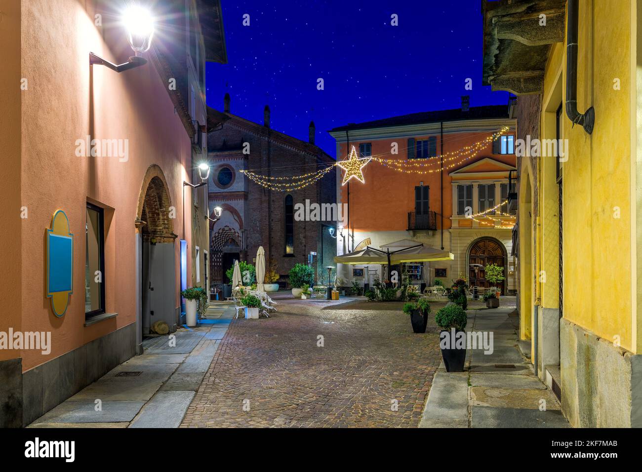 View of narrow cobblestone street among old buildings and Christmas illumination in the evening in Alba, Piedmont, Northern Italy. Stock Photo