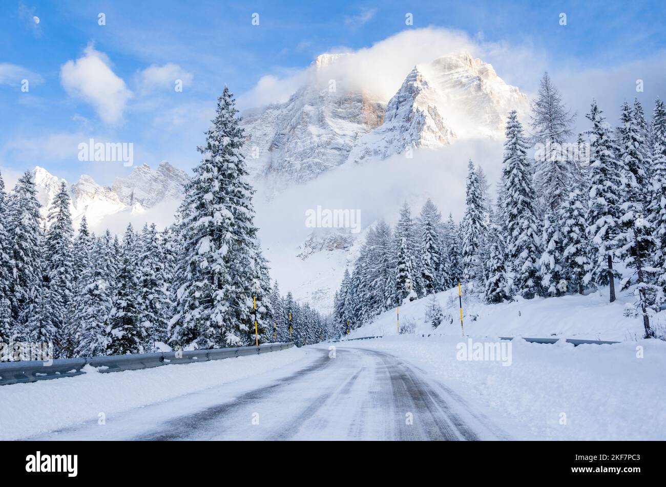 Icy road running through a snowy forest at the foot of a towering mountain on a winter day Stock Photo