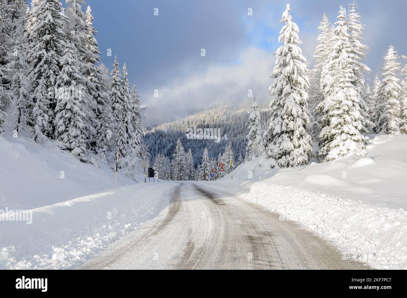 Deserted icy road through a snowy forest on a sunny winter day Stock Photo