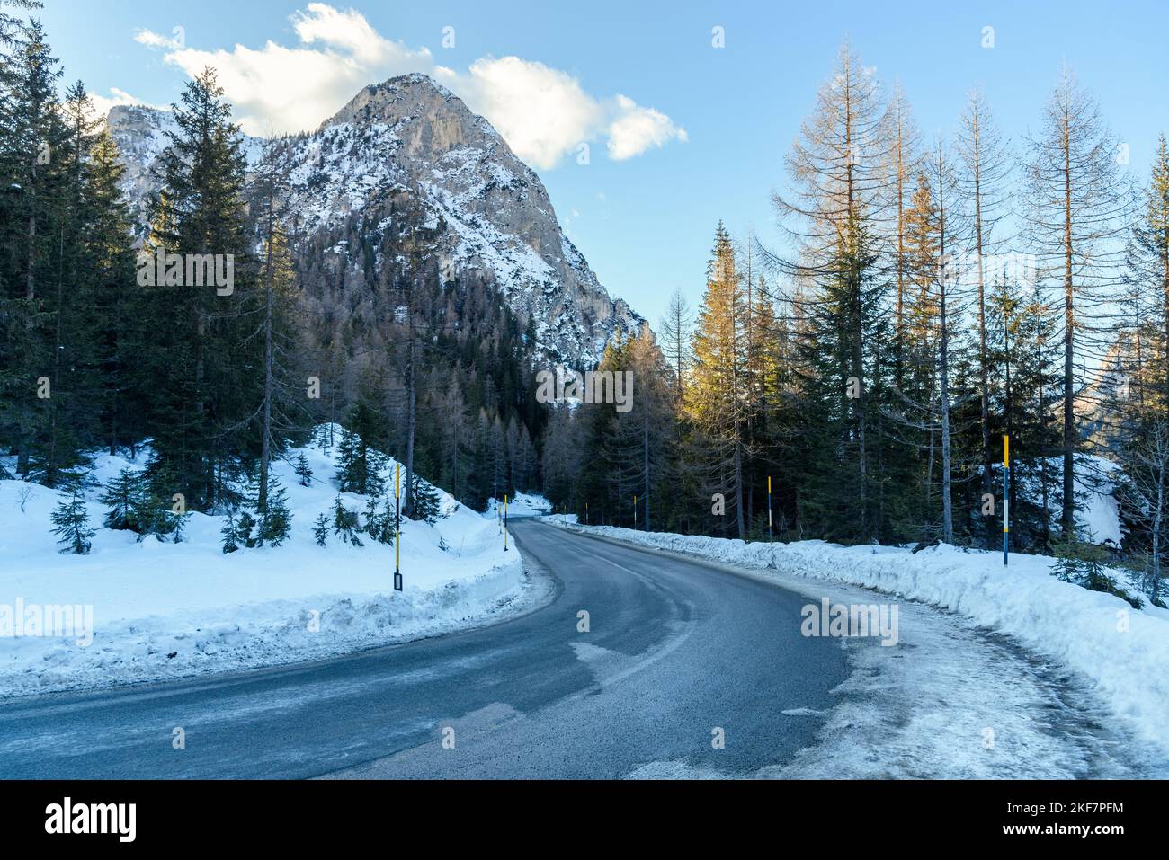 Empty icy mountain road through a snowy forest at sunset in winter Stock Photo
