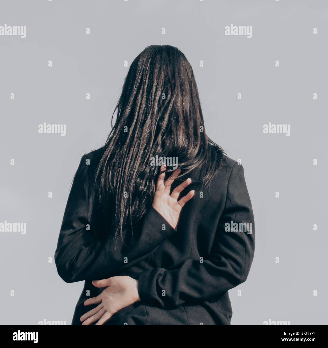 A person with long dark hair puts their hands behind their back