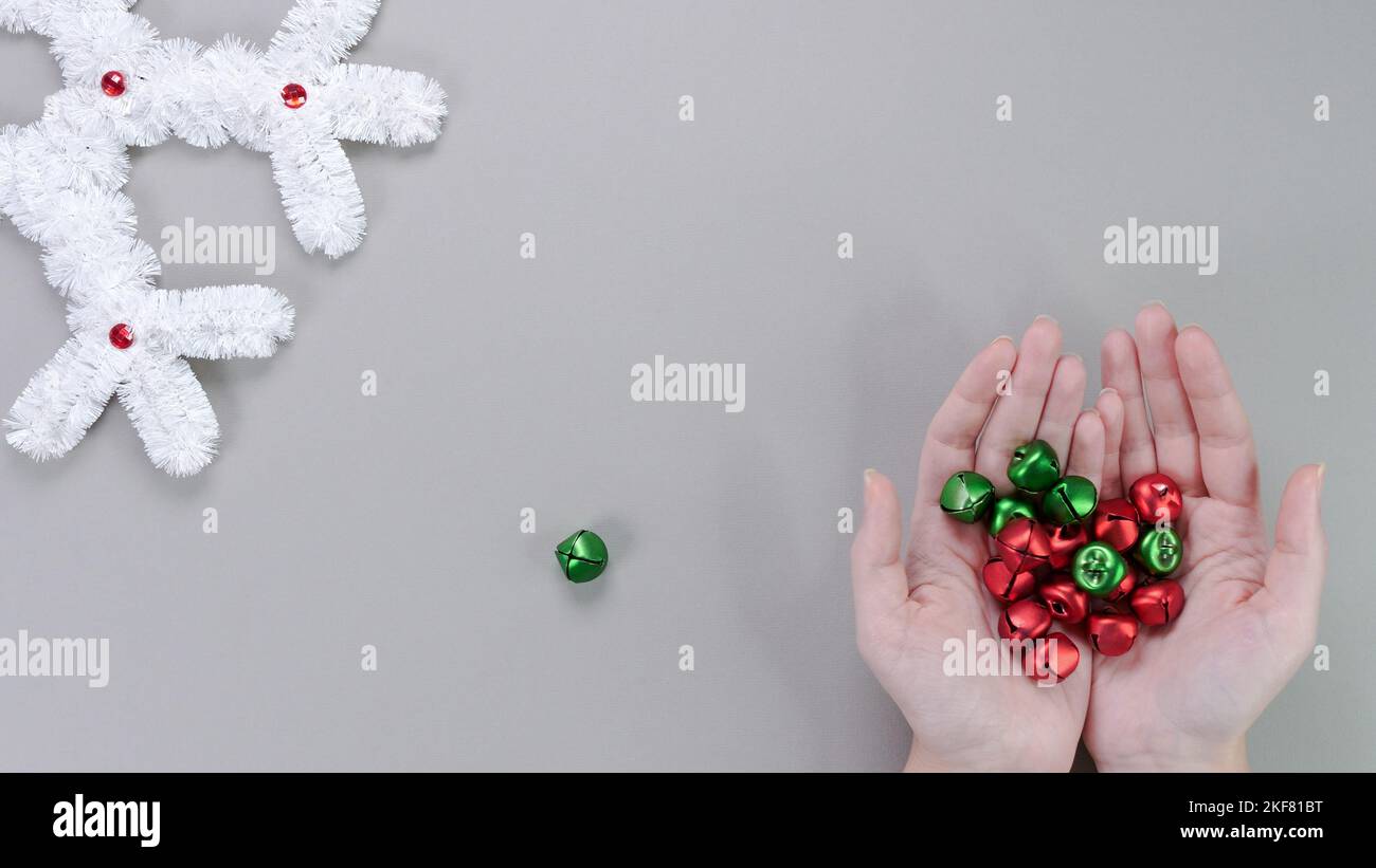 Female hands hold Christmas red green bells on a gray background with New Year's big white snowflake decor. The concept of New Year and Christmas holi Stock Photo