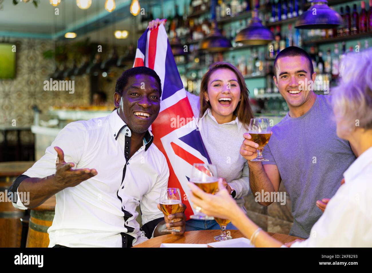 Happy sport fans holding flag of the Great Britain, celebrating victory of national team, drinking alcoholic drinks in pub Stock Photo