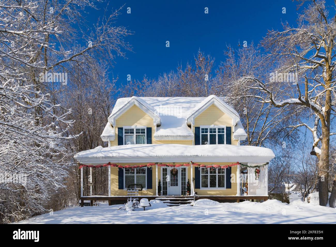 Yellow clapboard with blue and white trim cottage style home facade with Christmas decorations in winter. Stock Photo