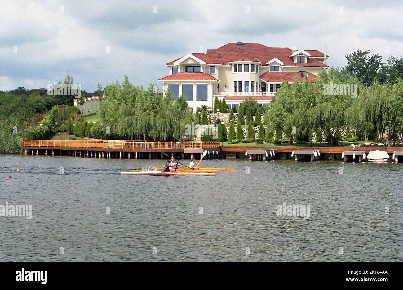 Ilfov County, Romania, approx. 2000. People kayaking on Lake Snagov, passing by a large new residential villa. Stock Photo
