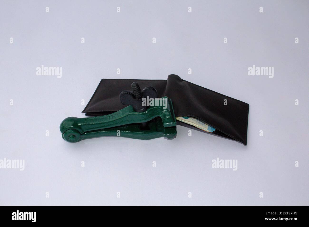 Image of a clamp that keeps a wallet closed and blocked from which banknotes come out. Reference to the global crisis, rising prices and savings Stock Photo