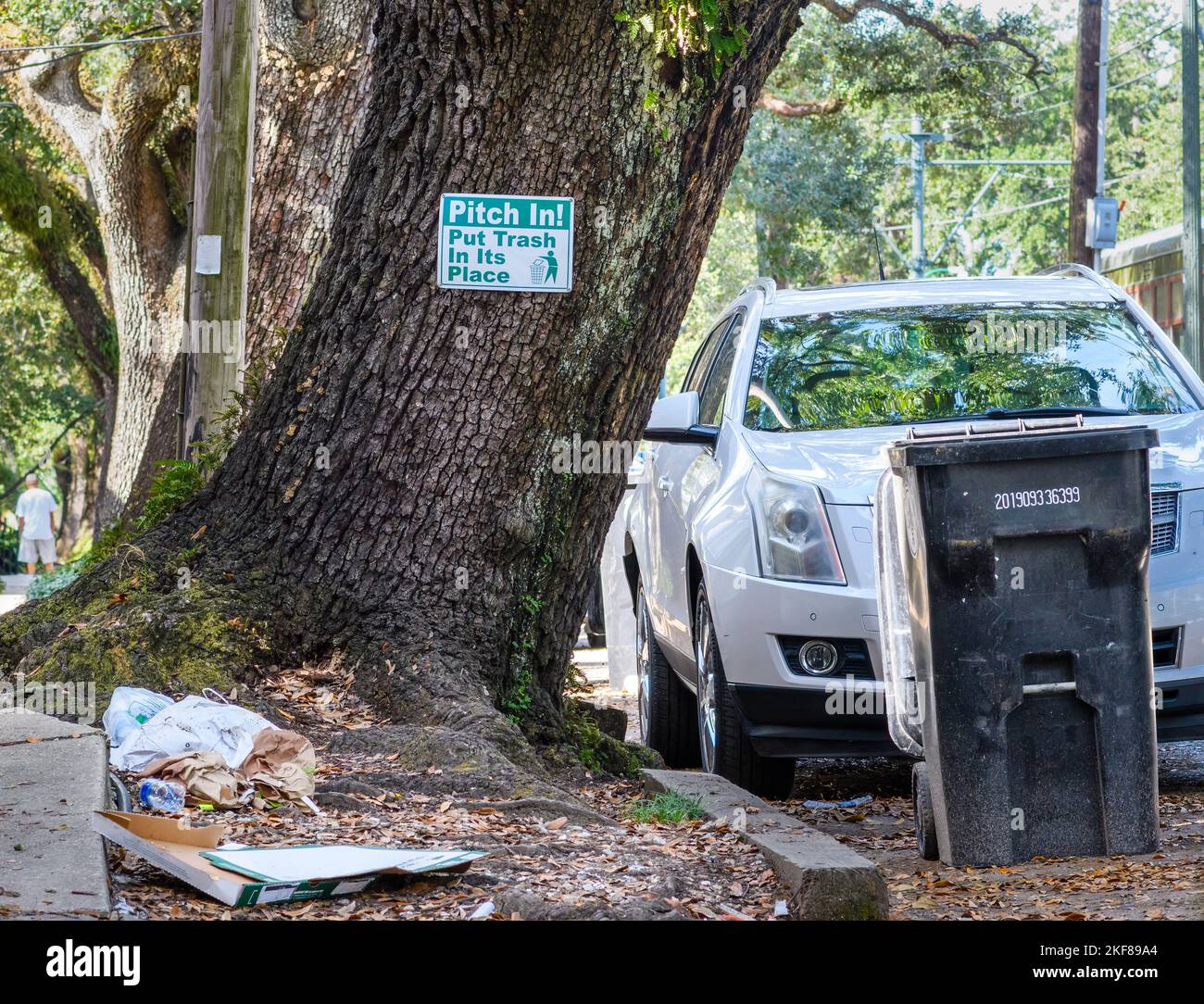 NEW ORLEANS, LA, USA - NOVEMBER 9, 2022: 'Pitch In! Put Trash in its Place' sign, litter along the sidewalk and trash cart in the street Stock Photo