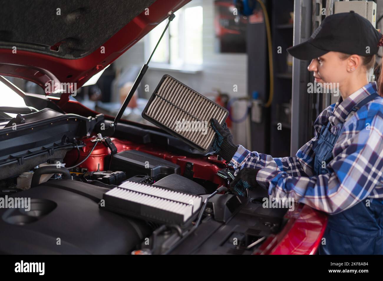 Caucasian female auto mechanic changes the engine air filter in the car. Stock Photo