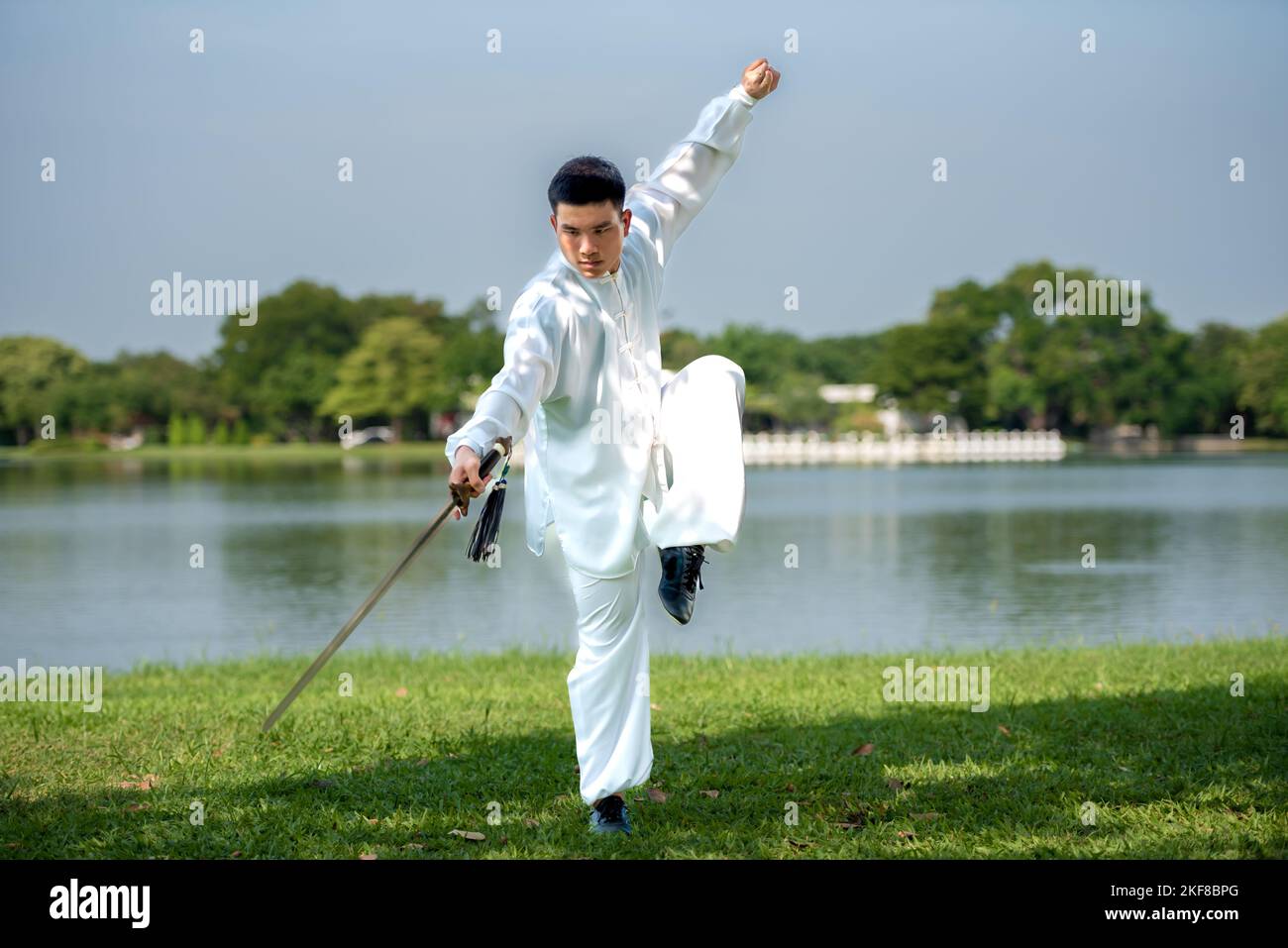 Young man practicing traditional Tai Chi Sword, Tai Ji in the park for healthy, traditional chinese martial arts concept on natural background . Stock Photo
