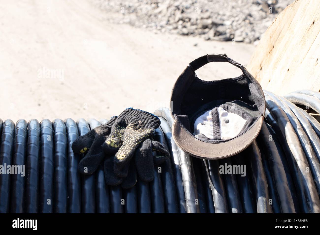 baseball cap and construction gloves lie on a black cable left by the builder in the sun Stock Photo