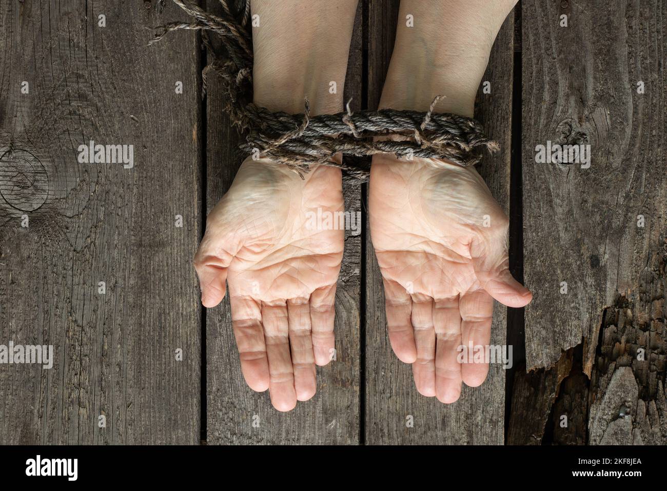 tied hands with rope of old woman on wooden table Stock Photo