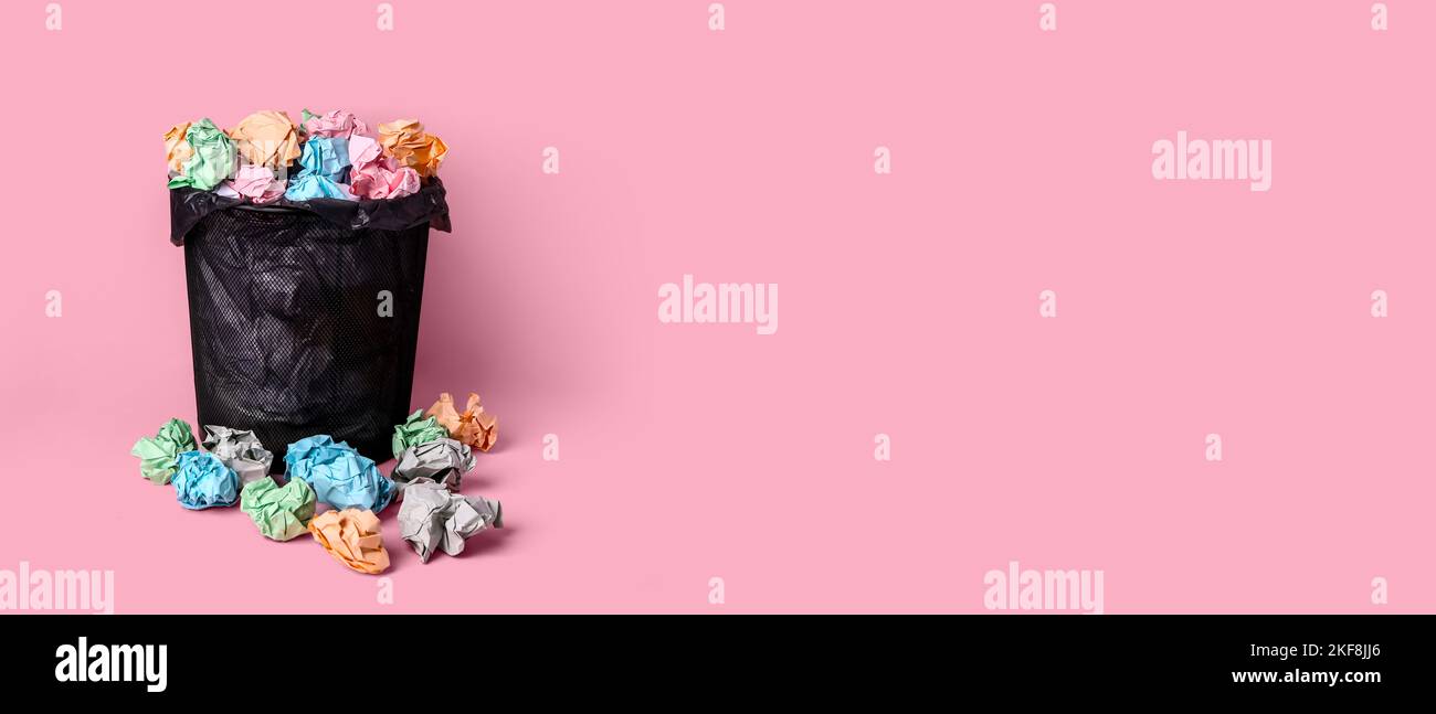 Trash bin full of crumpled paper on pink background with space for text