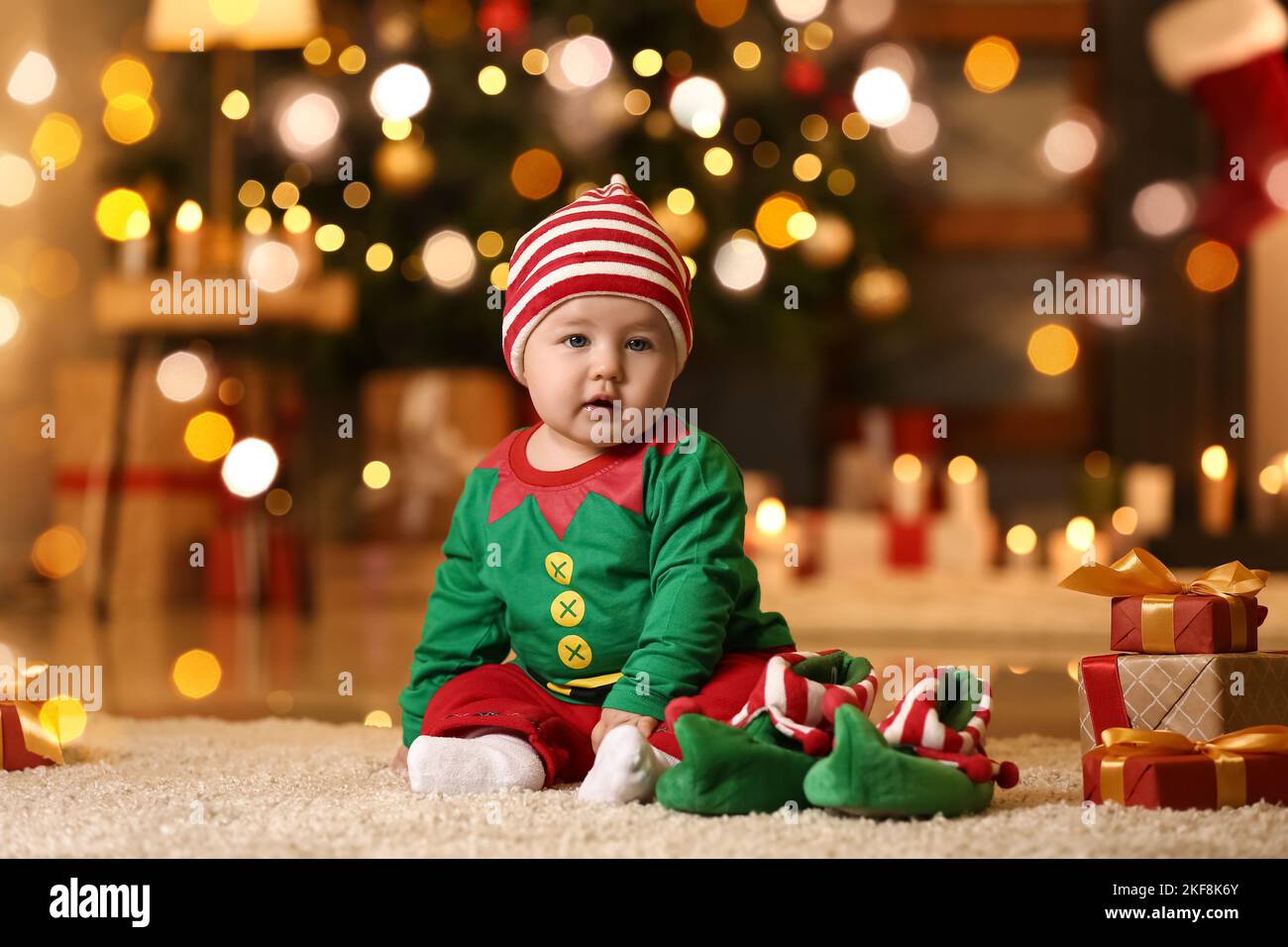Cute little baby in elf's costume and with gifts at home on Christmas