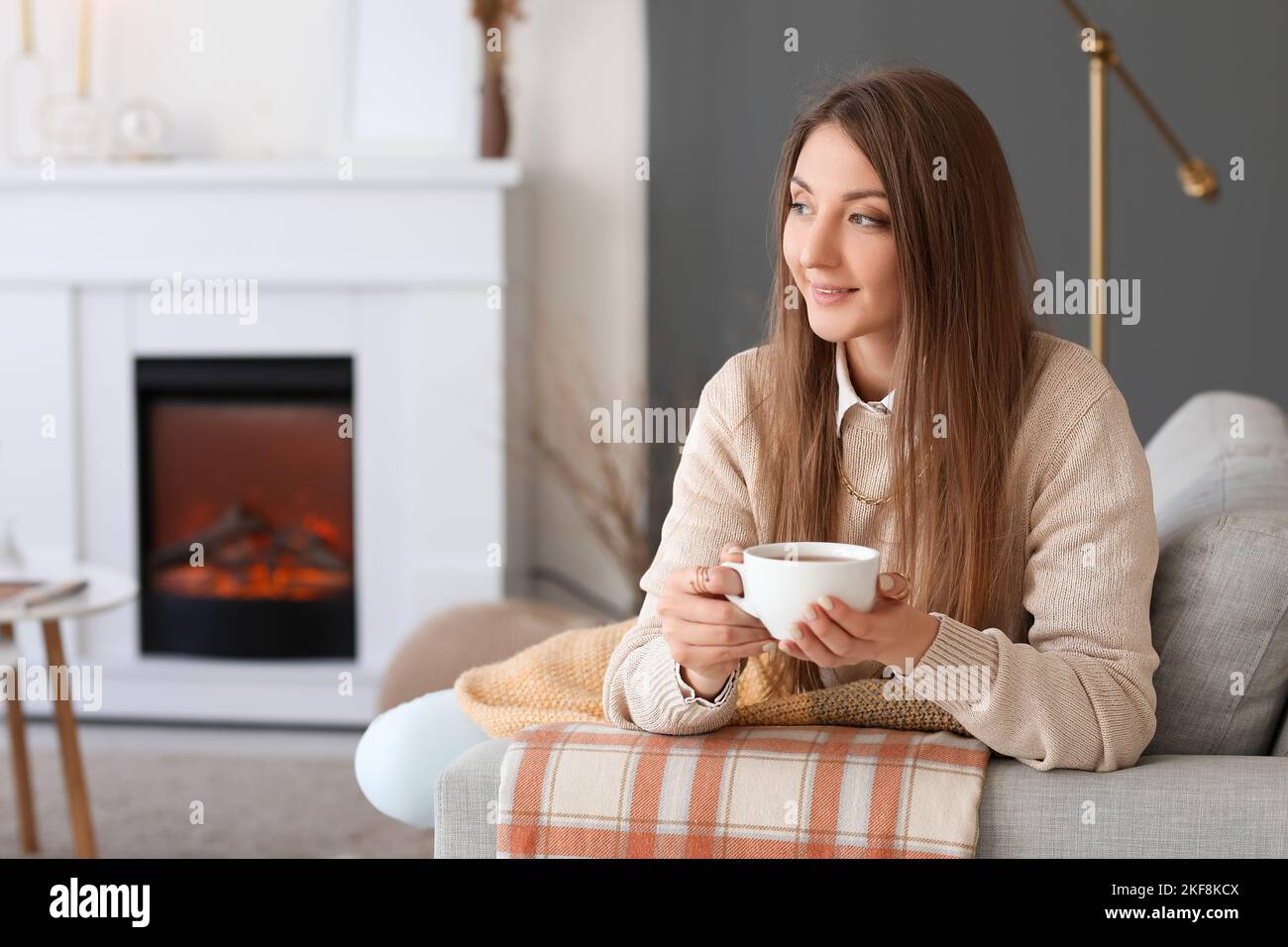 Young woman with cup of hot beverage sitting on sofa at home Stock ...