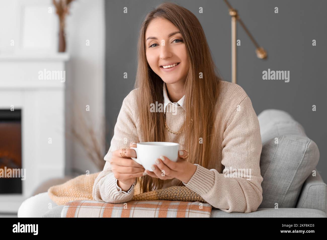 Young woman with cup of hot beverage sitting on sofa at home Stock ...