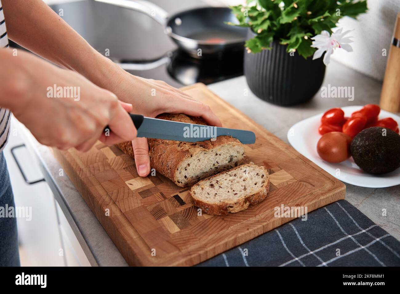 Woman cutting loaf of whole grain bread with large knife on cutting