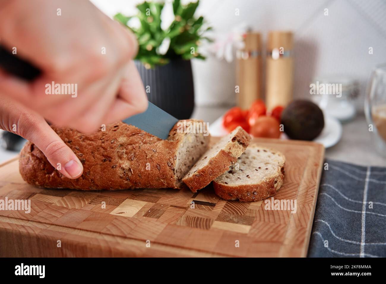 Woman cutting loaf of whole grain bread with large knife on cutting