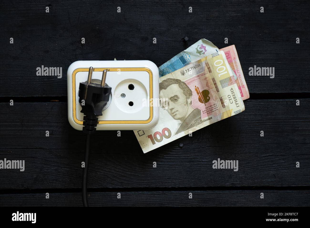 plastic razetkana on an old wooden wall and near 100 hryvnia, rising electricity prices, electricity prices, another rise in price Stock Photo