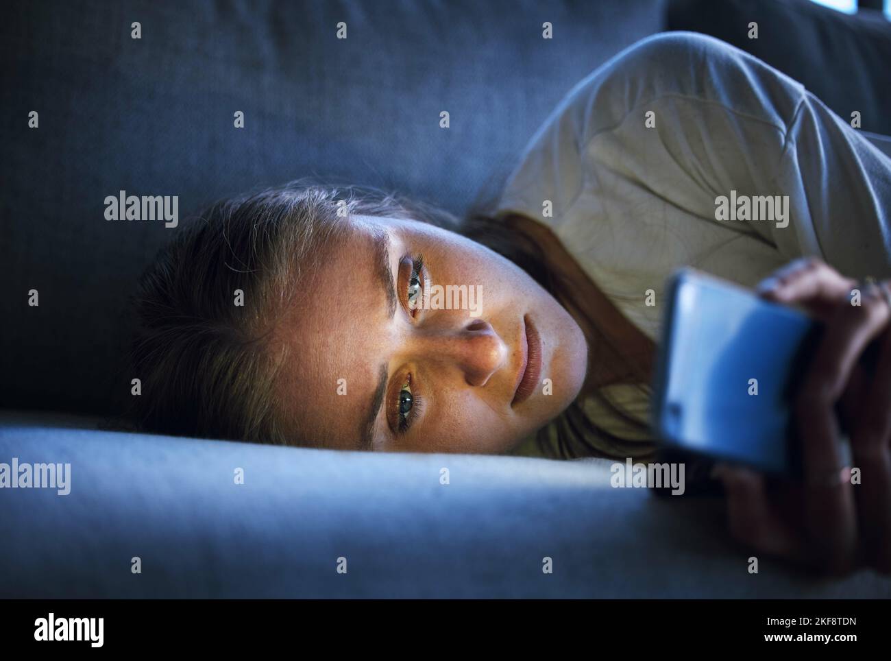 Phone, night and sad woman relaxing on sofa in living room scrolling on social media after a break up. Depression, upset and girl on couch in lounge Stock Photo