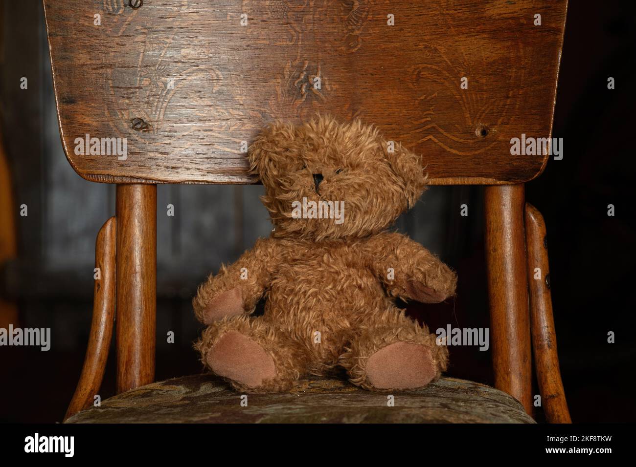 teddy brown bear sits on an old soft chair in the dark in the room at home, children's toy, teddy bear Stock Photo