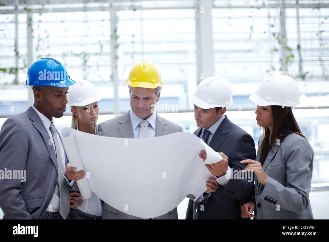 Making sure his design is perfect. A diverse group of serious-looking architects looking over blueprints together. Stock Photo